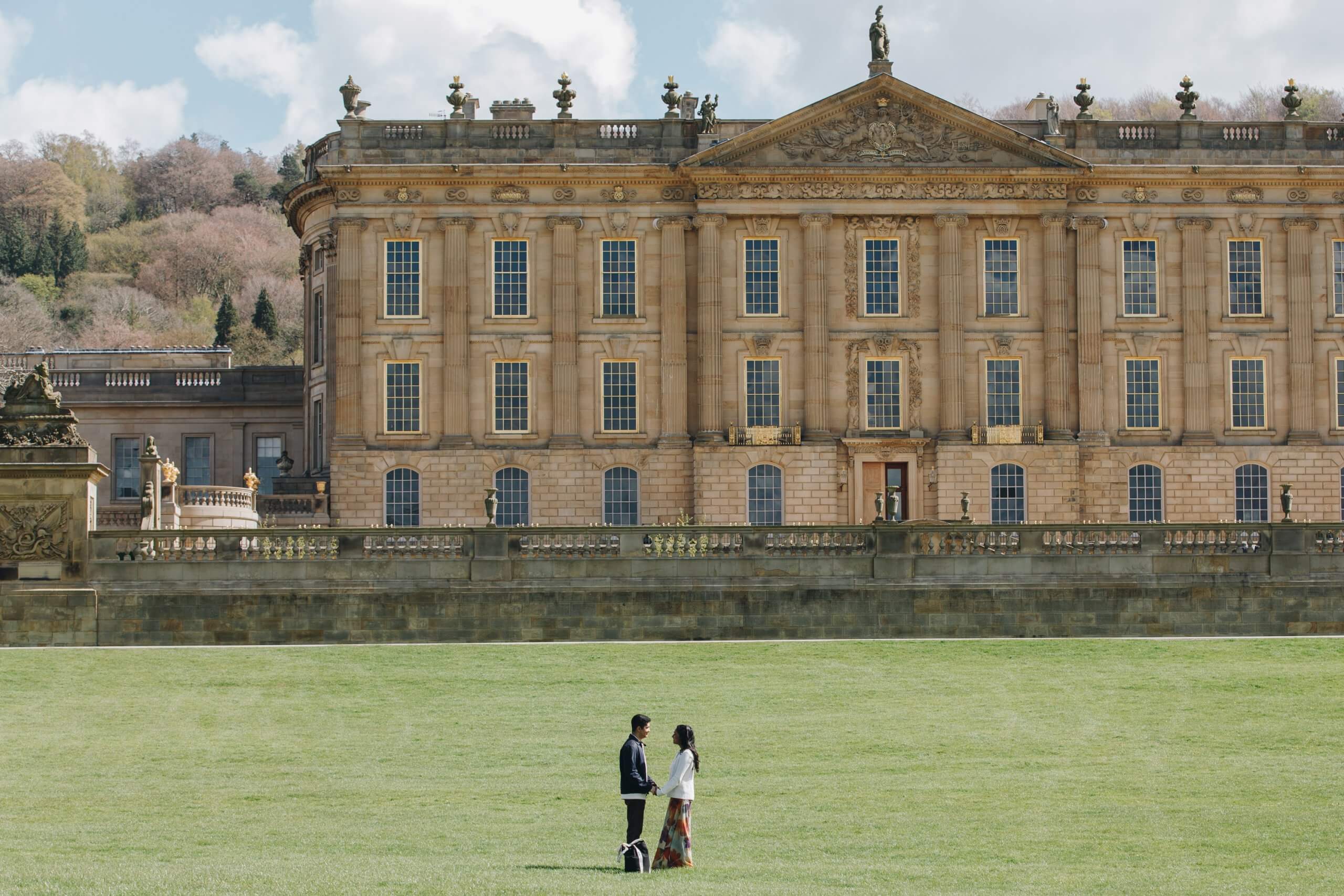 Chatsworth House exterior with couple celebrating engagement in foreground