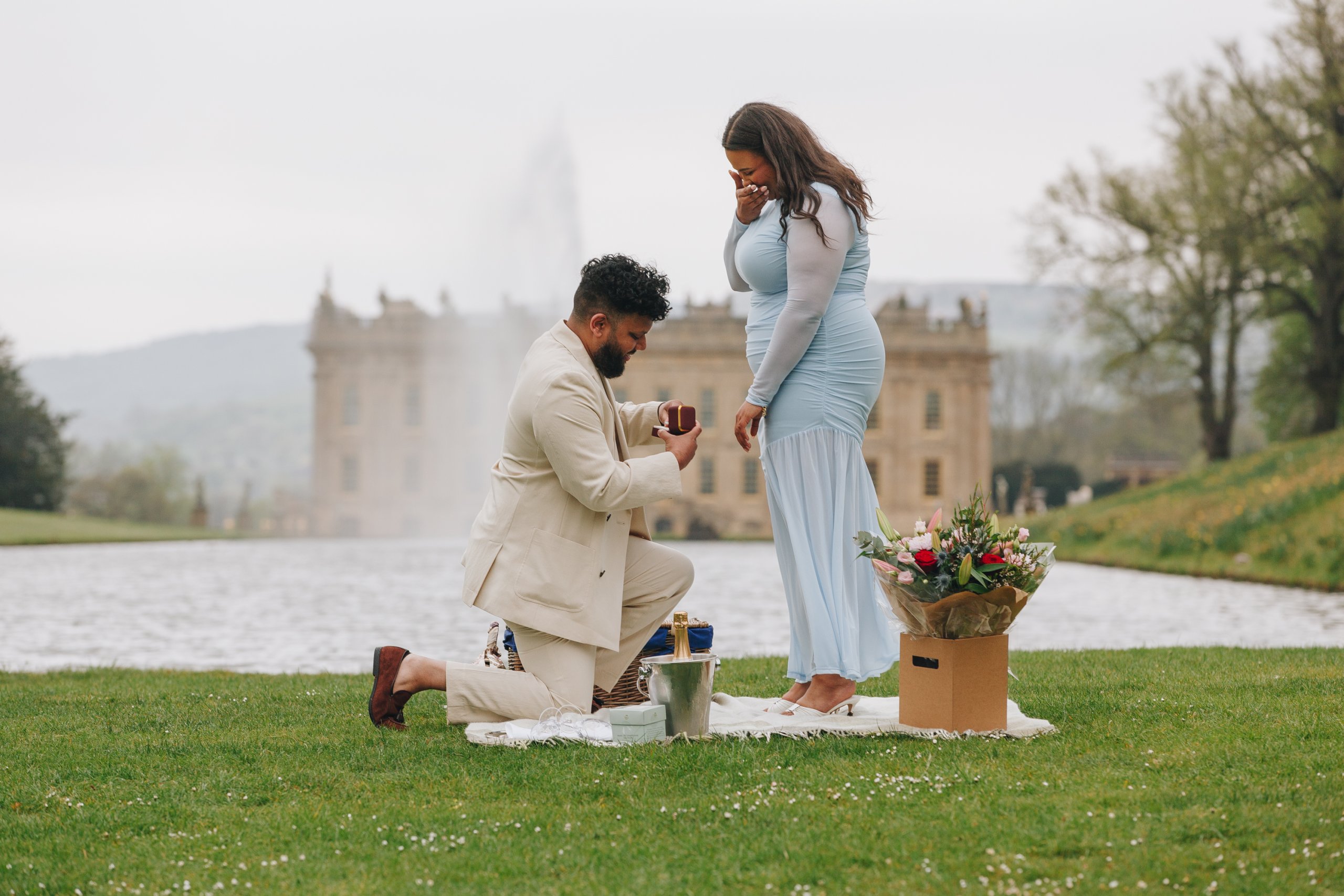 Surprise proposal at Chatsworth House garden with man kneeling and partner reacting